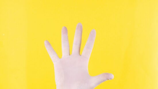 The close plan. A hand in white medical glove on a yellow background. The medicine. Place for an inscription. Medical gloves. Advertising