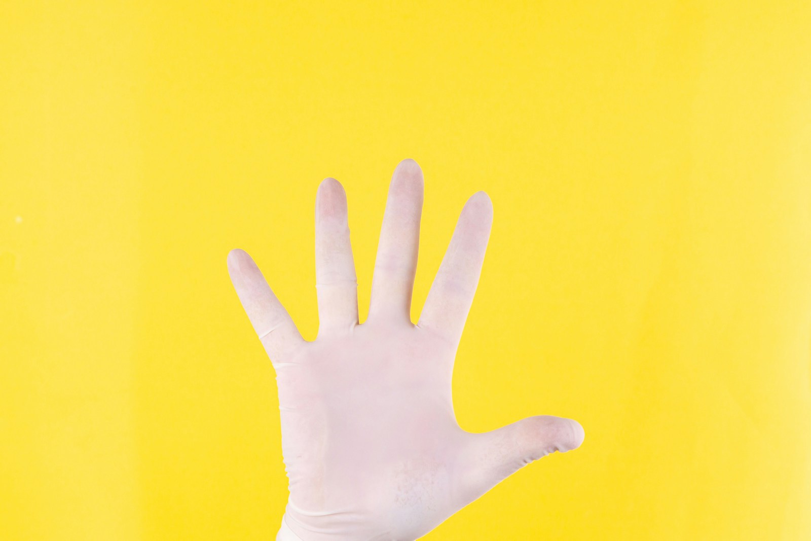 The close plan. A hand in white medical glove on a yellow background. The medicine. Place for an inscription. Medical gloves. Advertising