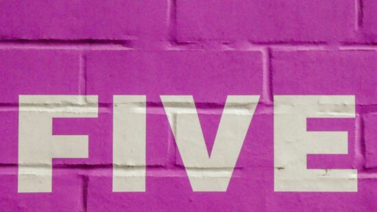 The word five in white letters on a pink brick wall.