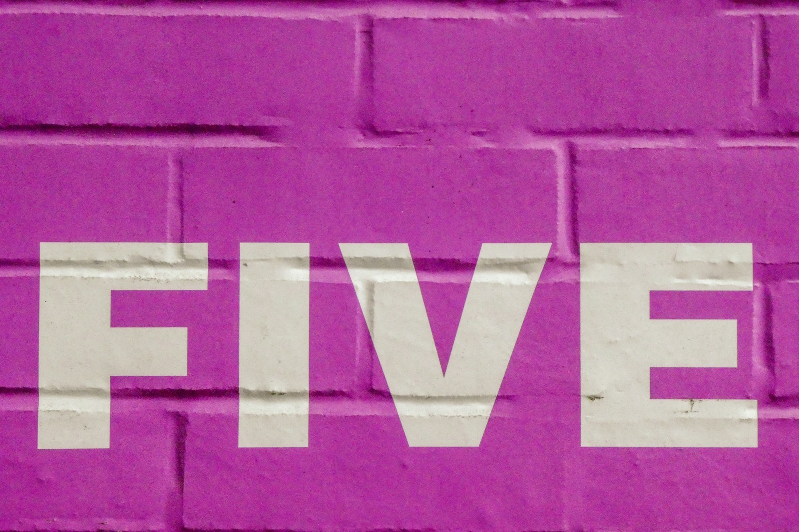The word five in white letters on a pink brick wall.